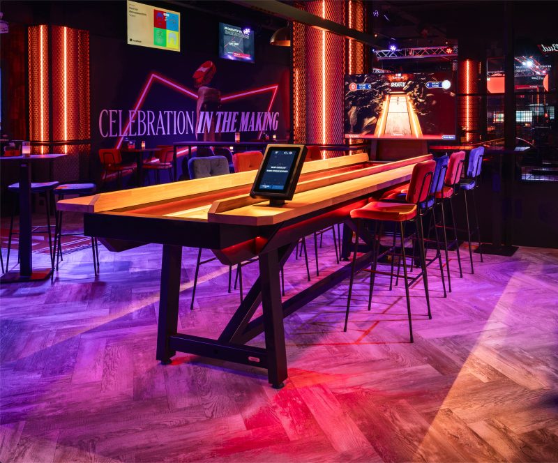 Salle de shuffleboard interactif, tables en bois et ambiance néon